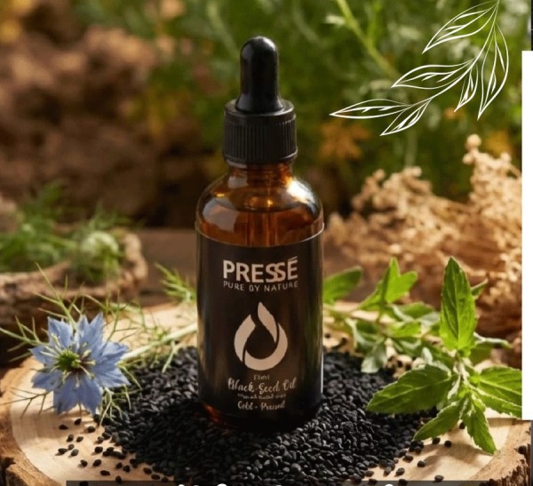 Pressé Black Seed Oil with its black label among black seeds and botanicals